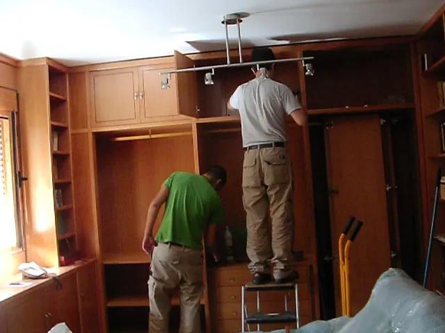 Dos carpinteros montando armarios y librerías de madera en una vivienda